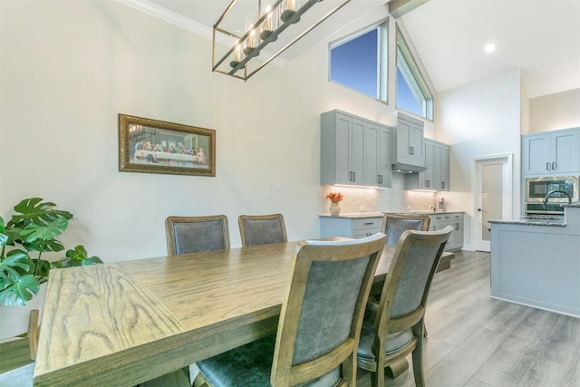 dining room featuring a towering ceiling, ornamental molding, and light wood-type flooring