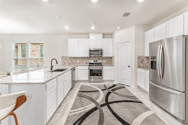 kitchen with light stone counters, kitchen peninsula, sink, white cabinetry, and appliances with stainless steel finishes