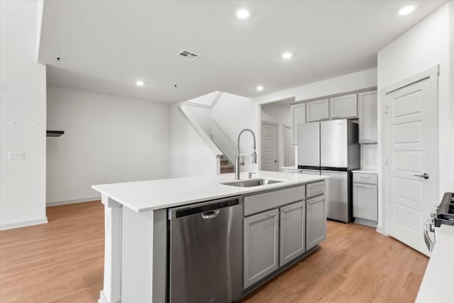 kitchen featuring gray cabinetry, appliances with stainless steel finishes, light hardwood / wood-style floors, and a kitchen island with sink