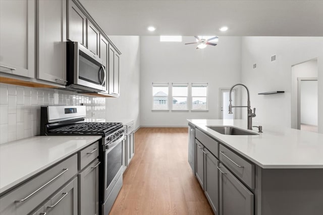 kitchen featuring light hardwood / wood-style floors, stainless steel appliances, sink, gray cabinetry, and a kitchen island with sink