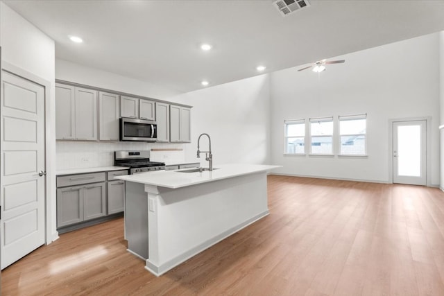 kitchen with stainless steel appliances, sink, a kitchen island with sink, light hardwood / wood-style flooring, and gray cabinets