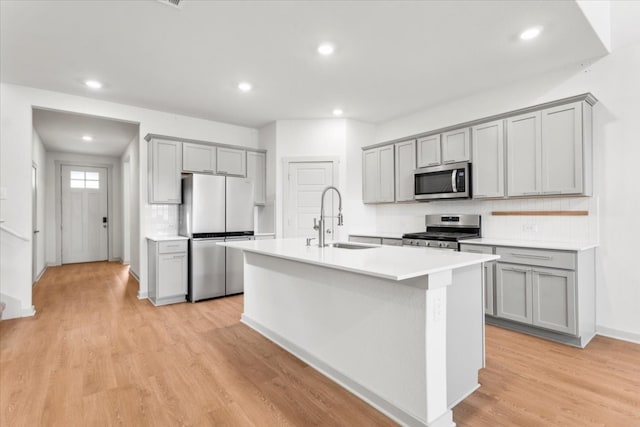 kitchen featuring light wood-type flooring, appliances with stainless steel finishes, sink, and a center island with sink