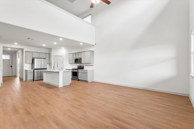 kitchen featuring a high ceiling, appliances with stainless steel finishes, an island with sink, and light hardwood / wood-style flooring