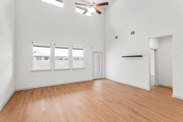 unfurnished living room featuring light hardwood / wood-style flooring, ceiling fan, and a towering ceiling