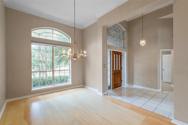 entrance foyer featuring light wood-type flooring, a towering ceiling, a notable chandelier, and crown molding