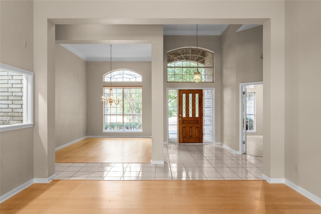 entryway with light wood-type flooring, crown molding, and a notable chandelier