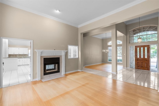 entrance foyer with a towering ceiling, a chandelier, crown molding, a tile fireplace, and light wood-type flooring