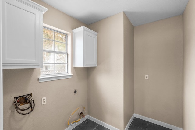 clothes washing area with cabinets, electric dryer hookup, and dark tile patterned floors