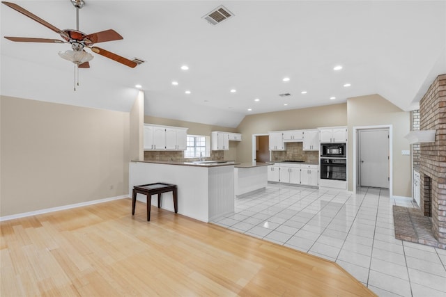 kitchen with black appliances, kitchen peninsula, lofted ceiling, white cabinets, and a brick fireplace