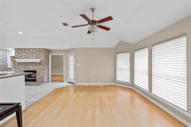 unfurnished living room featuring a fireplace, ceiling fan, light hardwood / wood-style flooring, and vaulted ceiling