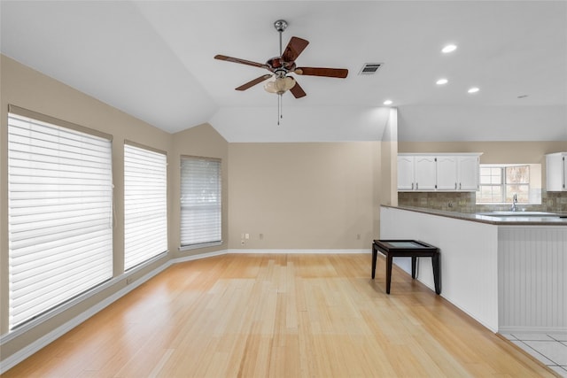 unfurnished living room with ceiling fan, sink, light wood-type flooring, and lofted ceiling