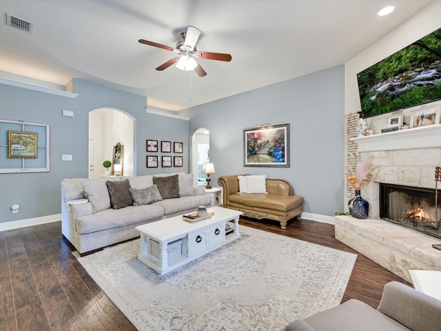 living room featuring ceiling fan, dark hardwood / wood-style floors, and a stone fireplace