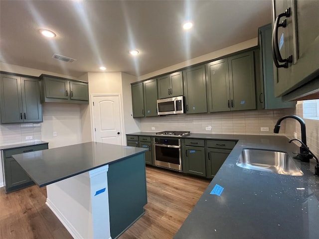 kitchen with sink, hardwood / wood-style flooring, stainless steel appliances, and green cabinets