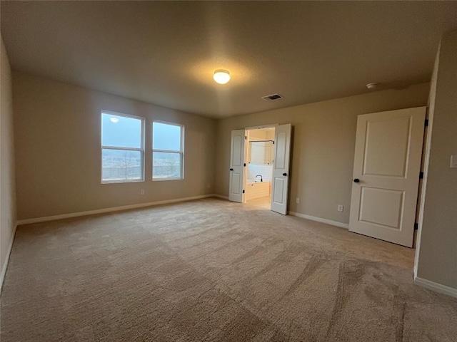 unfurnished bedroom featuring light colored carpet and ensuite bath