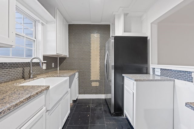 kitchen with stainless steel refrigerator, white cabinetry, sink, dark tile patterned floors, and light stone countertops