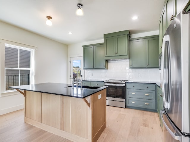 kitchen with light hardwood / wood-style floors, stainless steel appliances, decorative backsplash, sink, and an island with sink