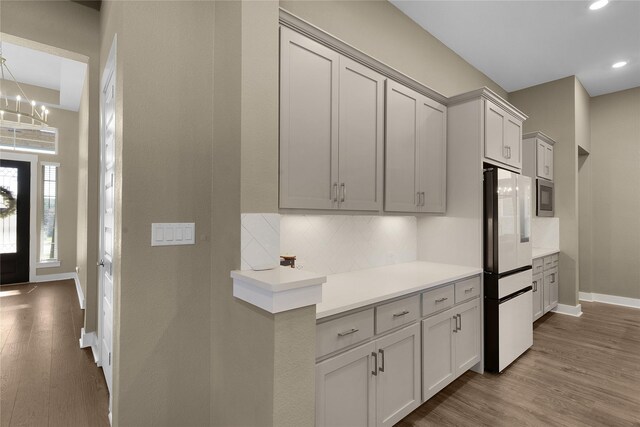 kitchen with a notable chandelier, stainless steel microwave, light hardwood / wood-style floors, tasteful backsplash, and white refrigerator