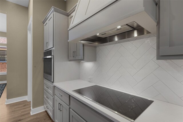 kitchen with custom range hood, tasteful backsplash, oven, gray cabinetry, and black electric cooktop