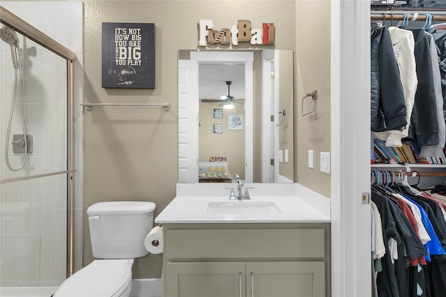 bathroom with toilet, a shower with shower door, ceiling fan, and vanity