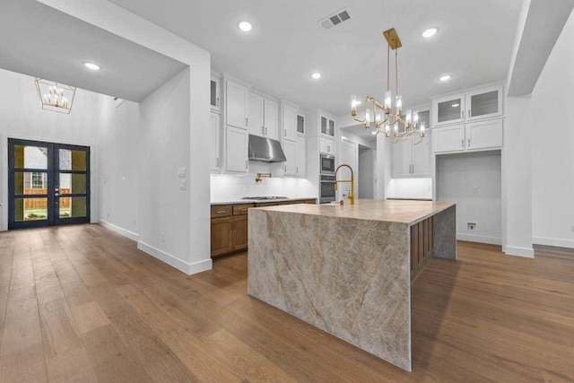 kitchen featuring french doors, a center island with sink, white cabinetry, light stone countertops, and hardwood / wood-style floors