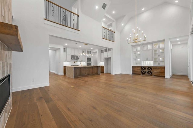 unfurnished living room featuring high vaulted ceiling, an inviting chandelier, sink, hardwood / wood-style floors, and a tile fireplace