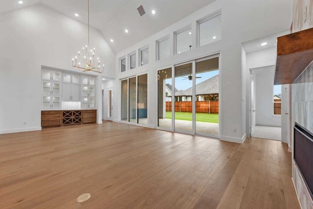 unfurnished living room featuring light hardwood / wood-style floors, high vaulted ceiling, and a notable chandelier