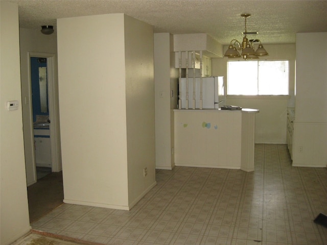 kitchen with a textured ceiling, white fridge, pendant lighting, and a notable chandelier