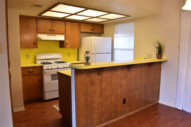 kitchen featuring kitchen peninsula, white appliances, a textured ceiling, and dark hardwood / wood-style flooring