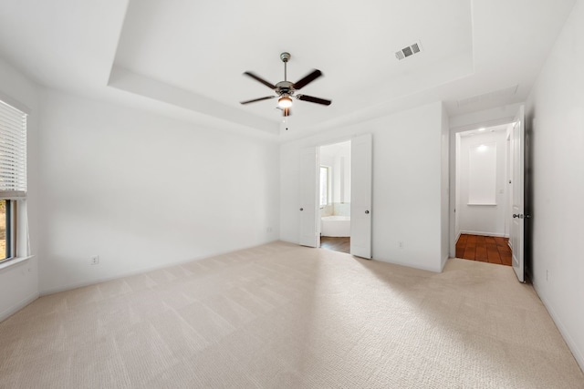 unfurnished bedroom with ceiling fan, connected bathroom, light carpet, and a tray ceiling