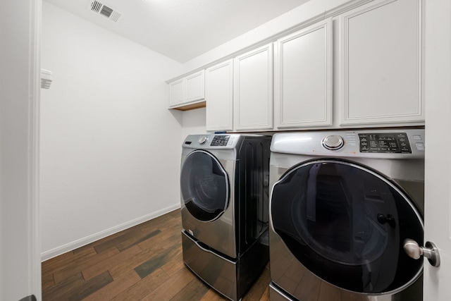 clothes washing area with cabinets, washing machine and clothes dryer, and dark hardwood / wood-style floors