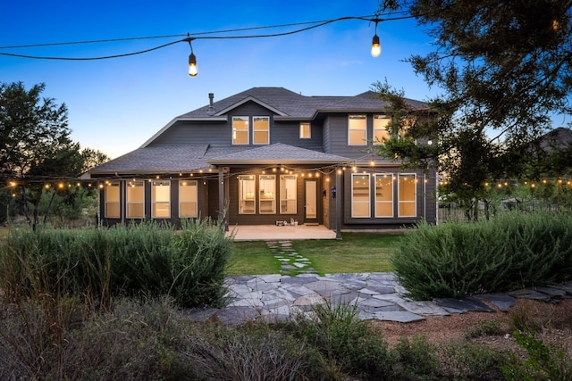 back house at dusk with a patio and a yard