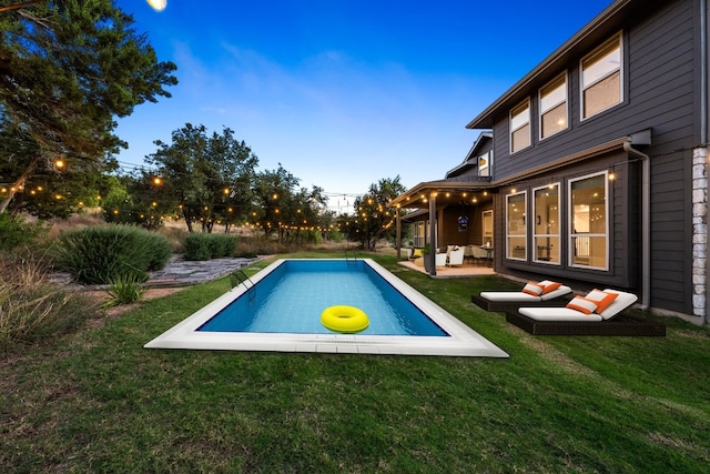 pool at dusk featuring a lawn and a patio