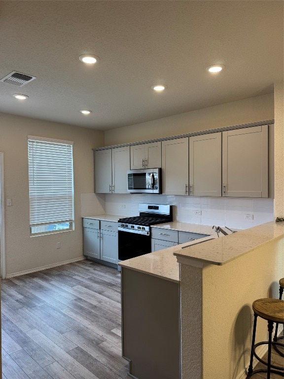 kitchen with kitchen peninsula, a breakfast bar area, gray cabinetry, light hardwood / wood-style flooring, and gas range oven