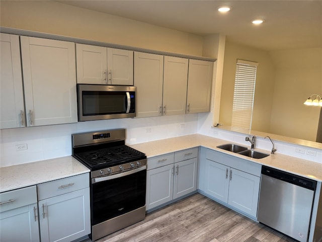 kitchen featuring light stone counters, sink, tasteful backsplash, light wood-type flooring, and appliances with stainless steel finishes