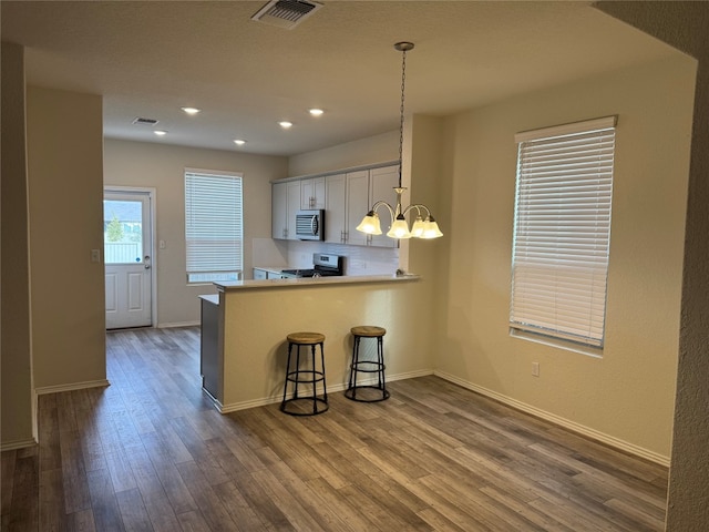 kitchen featuring decorative light fixtures, a breakfast bar, white cabinets, dark wood-type flooring, and kitchen peninsula