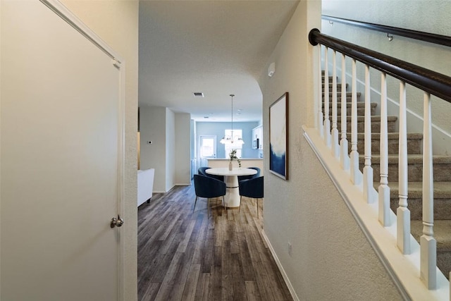 corridor featuring a chandelier, stairway, baseboards, and wood finished floors