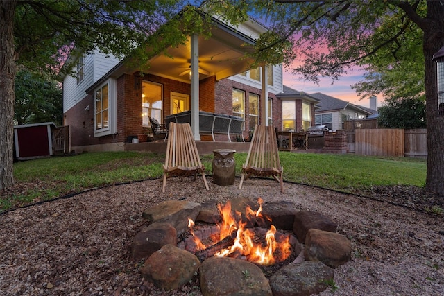 patio terrace at dusk featuring a lawn, ceiling fan, and an outdoor fire pit