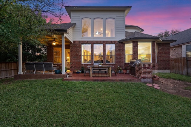 back house at dusk featuring a patio and a lawn