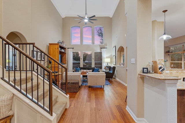 interior space with ceiling fan, light hardwood / wood-style flooring, crown molding, and a high ceiling