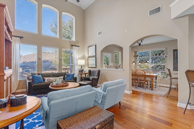 living room featuring a towering ceiling, light hardwood / wood-style flooring, and a healthy amount of sunlight