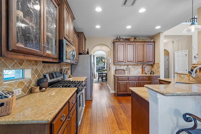 kitchen with sink, stainless steel appliances, light hardwood / wood-style flooring, backsplash, and pendant lighting