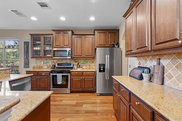 kitchen featuring decorative backsplash, light stone counters, light wood-type flooring, and appliances with stainless steel finishes