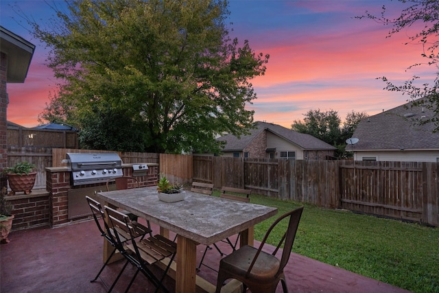 patio terrace at dusk featuring a lawn, area for grilling, and exterior kitchen