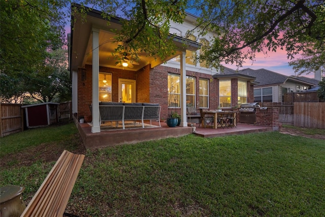 back house at dusk featuring exterior kitchen, a patio, and a yard