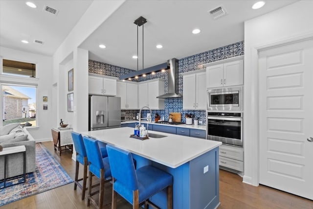 kitchen featuring a center island with sink, a breakfast bar area, stainless steel appliances, wall chimney range hood, and white cabinets