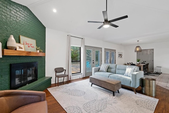 living room with hardwood / wood-style flooring, ceiling fan, a fireplace, vaulted ceiling, and french doors