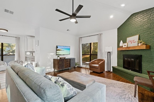 living room featuring lofted ceiling, dark wood-type flooring, ceiling fan, a fireplace, and brick wall