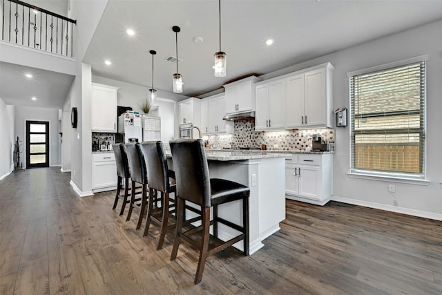 kitchen featuring white cabinetry, pendant lighting, an island with sink, a breakfast bar area, and dark wood-type flooring