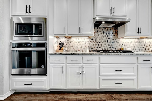 kitchen with extractor fan, appliances with stainless steel finishes, white cabinets, and light stone counters