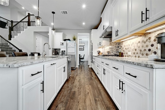 kitchen featuring white cabinetry, dark hardwood / wood-style flooring, pendant lighting, sink, and an island with sink